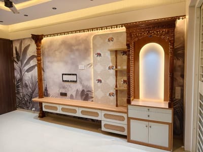 Carved wooden pooja unit with backlit arch beside a TV unit and elephant-motif tile panel
