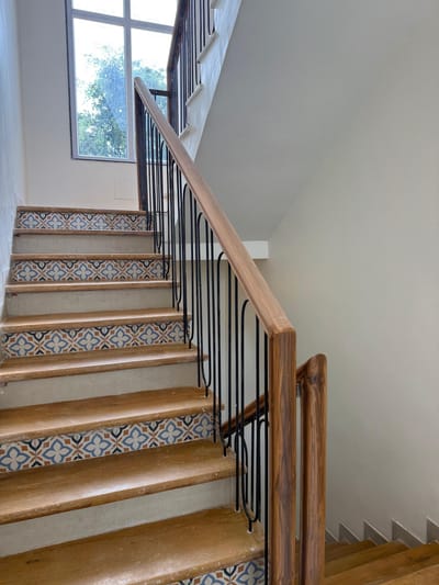 Staircase with wooden treads, patterned riser tiles and black metal railing
